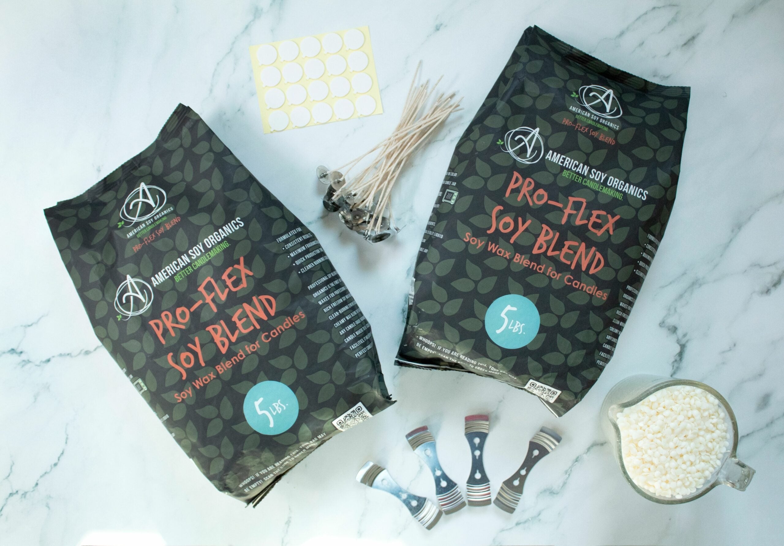 Two 5 lb. packages of Pro-Flex Soy Blend with wicks, adhesive rounds, wick holders and a glass container with wax beads, displayed on a marble surface.