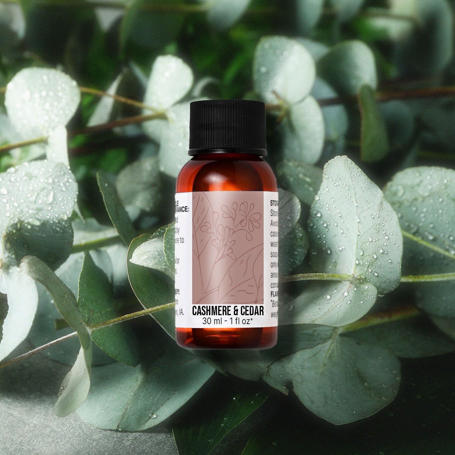 Bottle of Cashmere & Cedar fragrance oil on a background of eucalyptus leaves with water droplets.