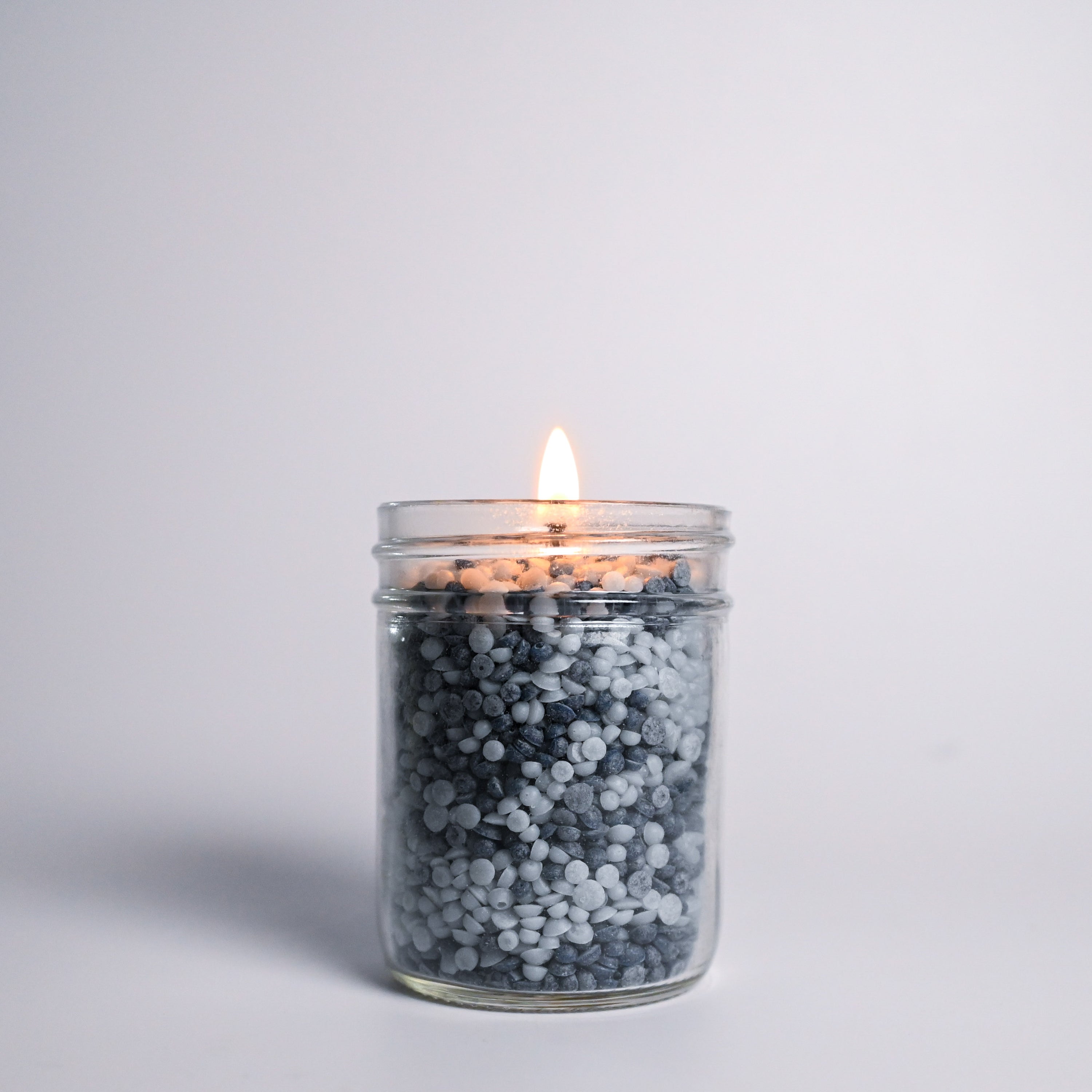 Candle in a glass jar with decorative wax beads on a light gray background