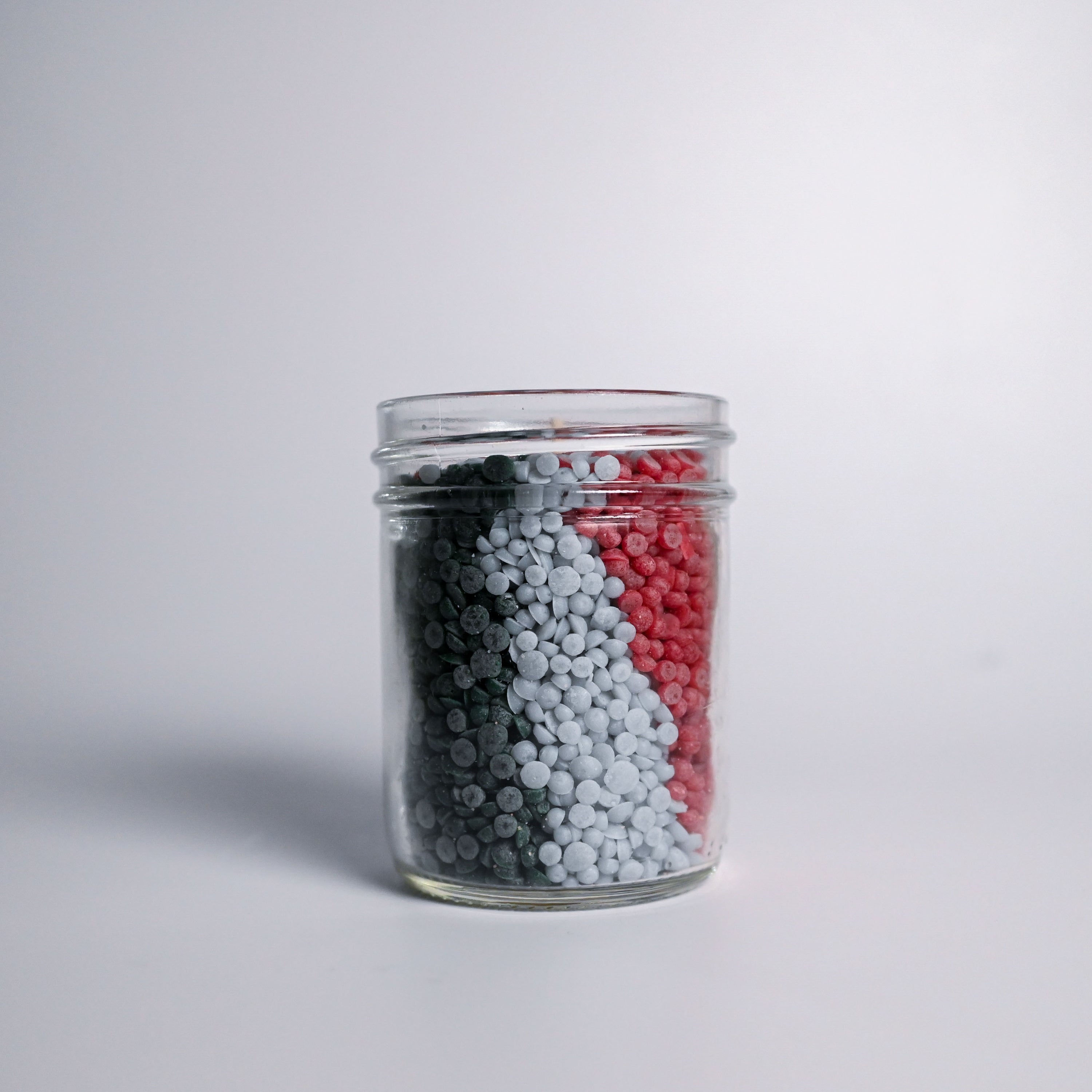 Glass jar filled with multicolored wax beads on a light gray background