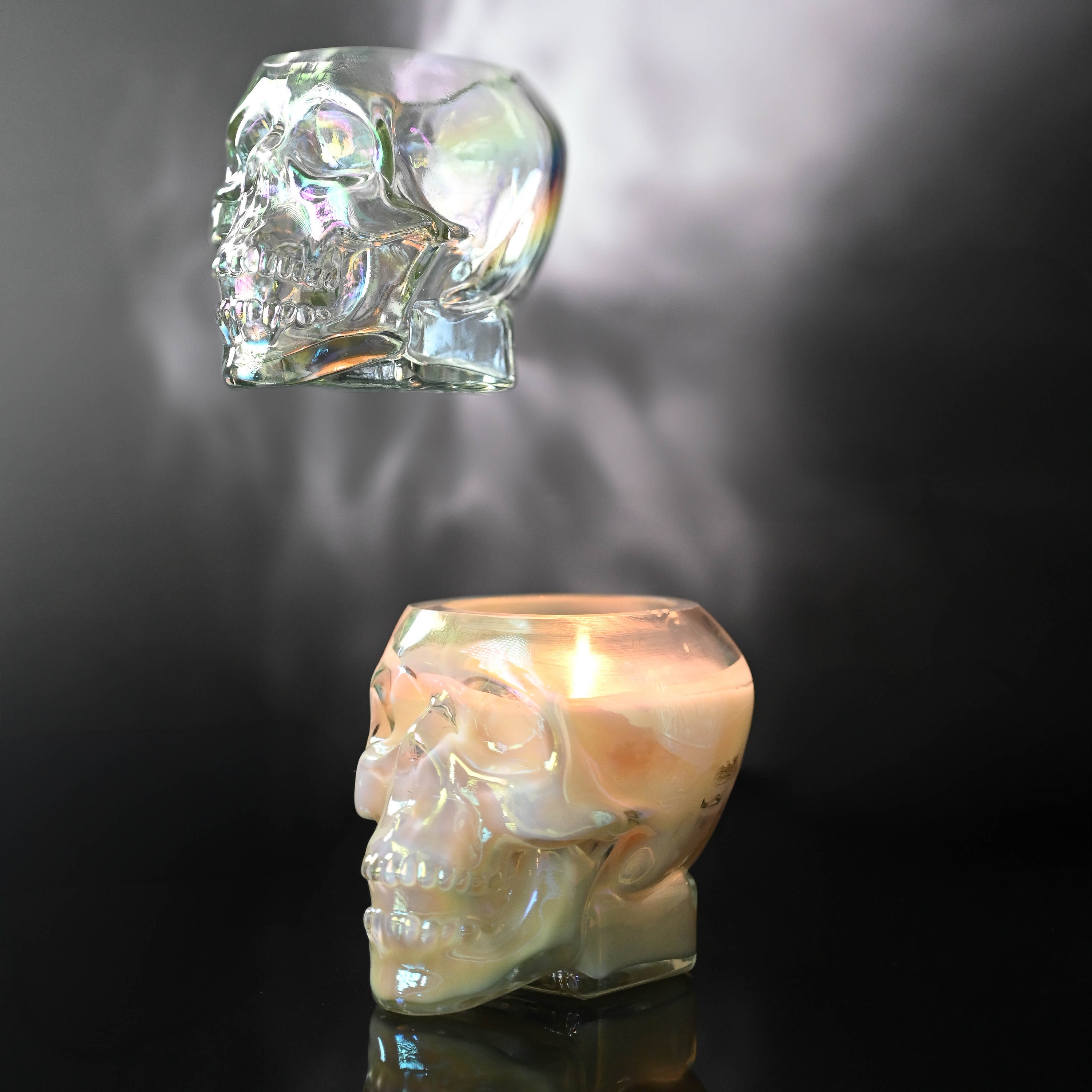 Iridescent glass skull candle jar with a lit candle on a dark background