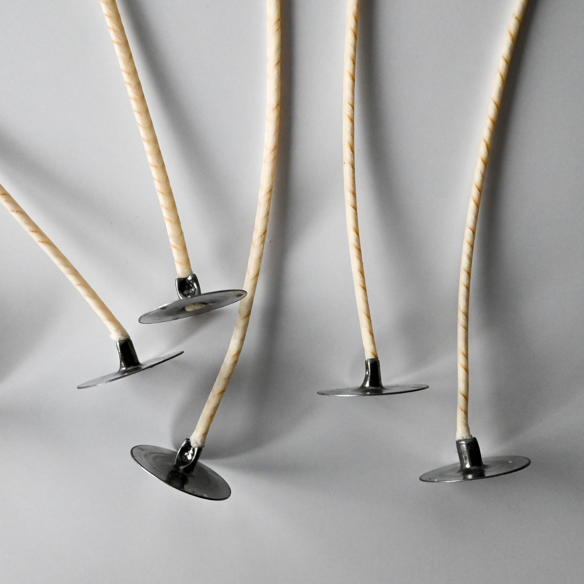 A collection of thin, twisted candle wicks positioned vertically on a white background