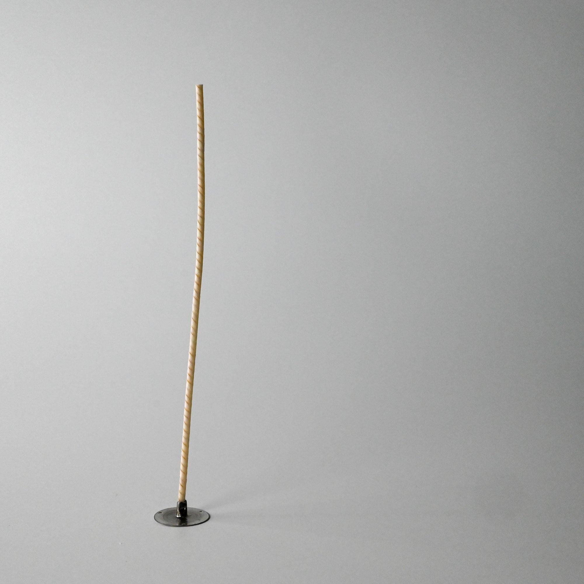 A tall beige wick standing upright in a small round black base against a white background
