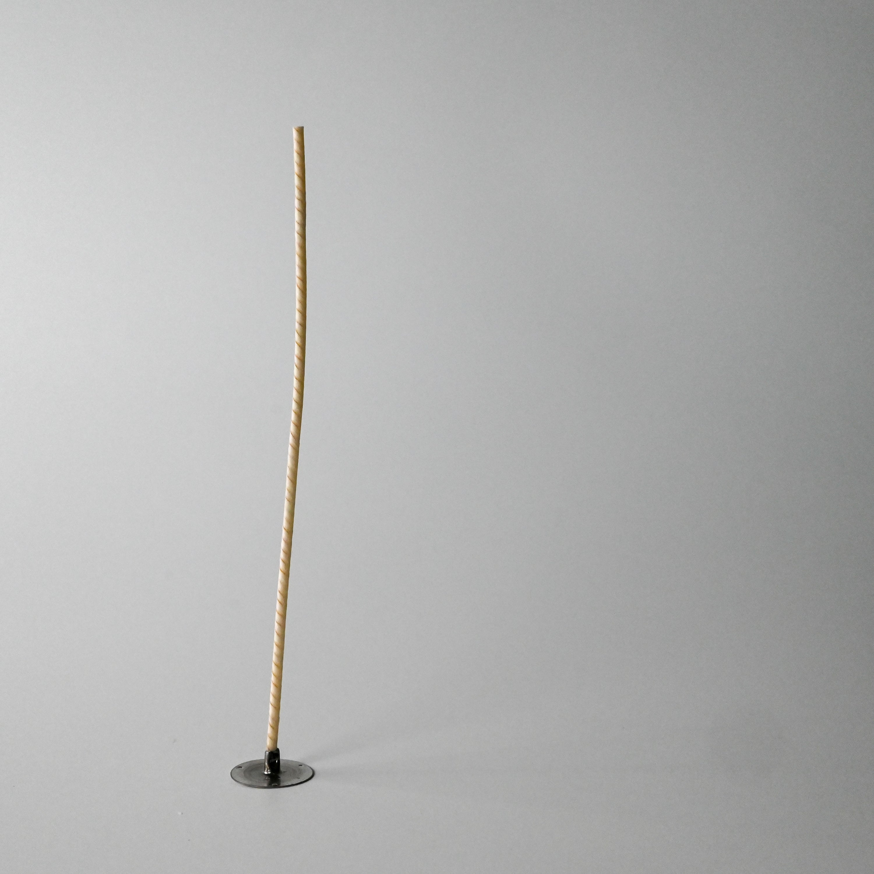 A tall beige wick standing upright in a small round black base against a white background