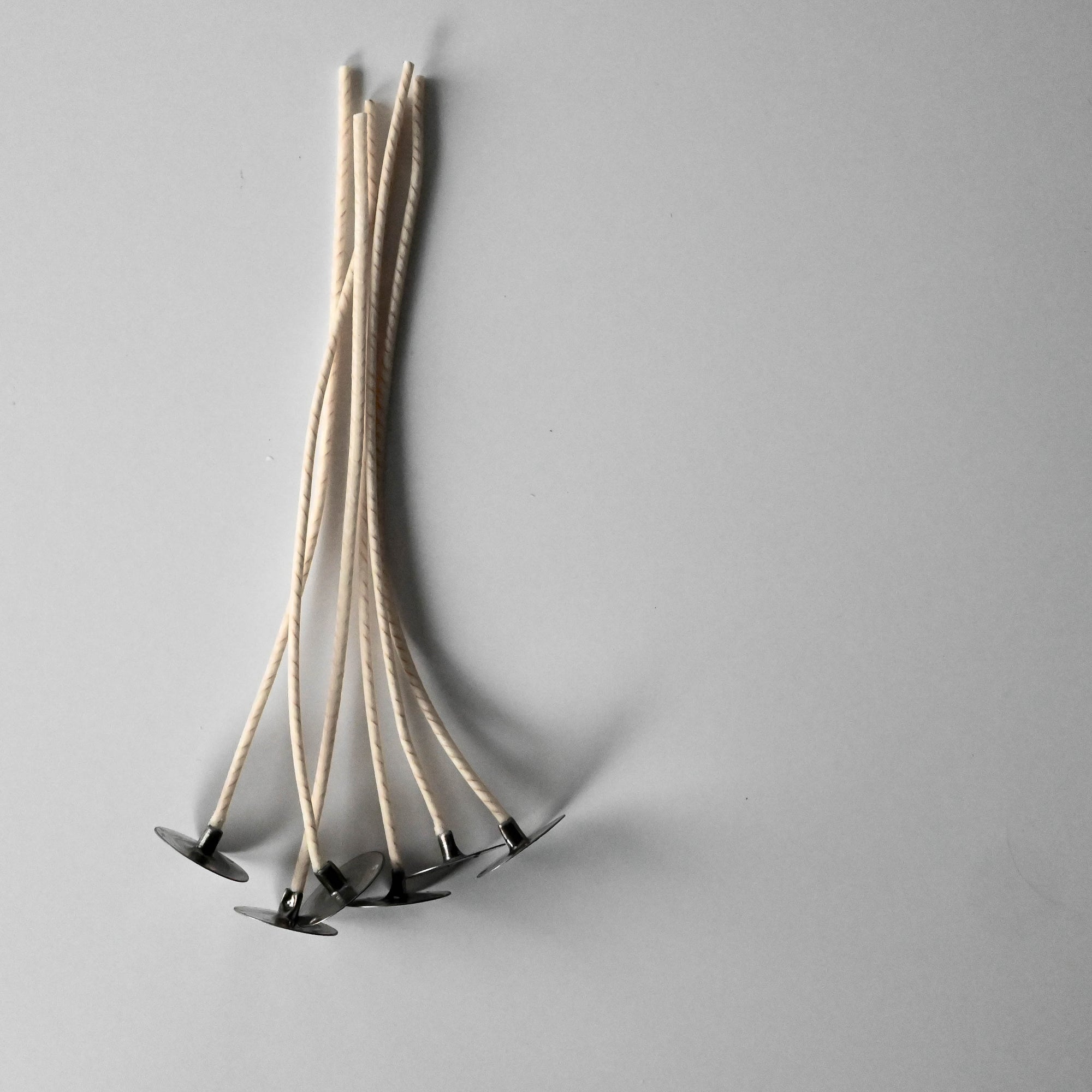 A collection of thin, twisted candle wicks positioned vertically on a plain white surface