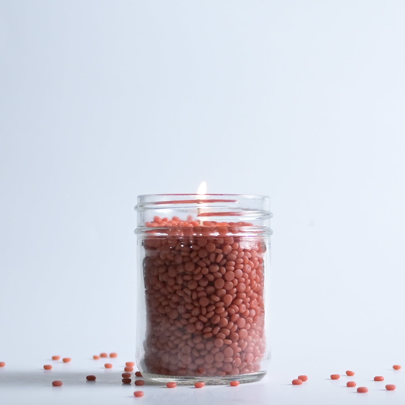 Jar filled with red wax beads on a light gray background
