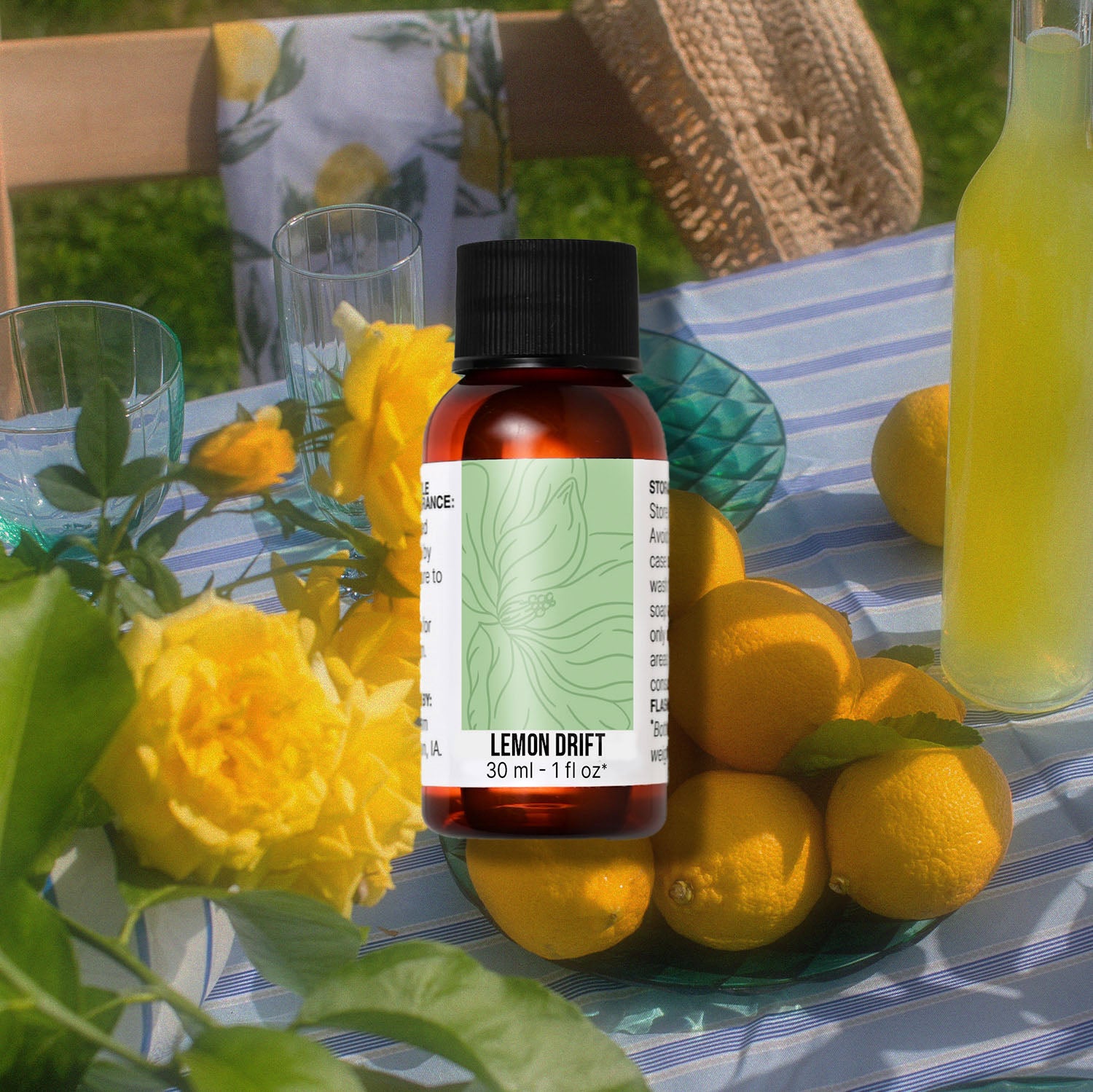 Bottle of 'Lemon Drift' fragrance oil with lemons and flowers on a table outdoors.