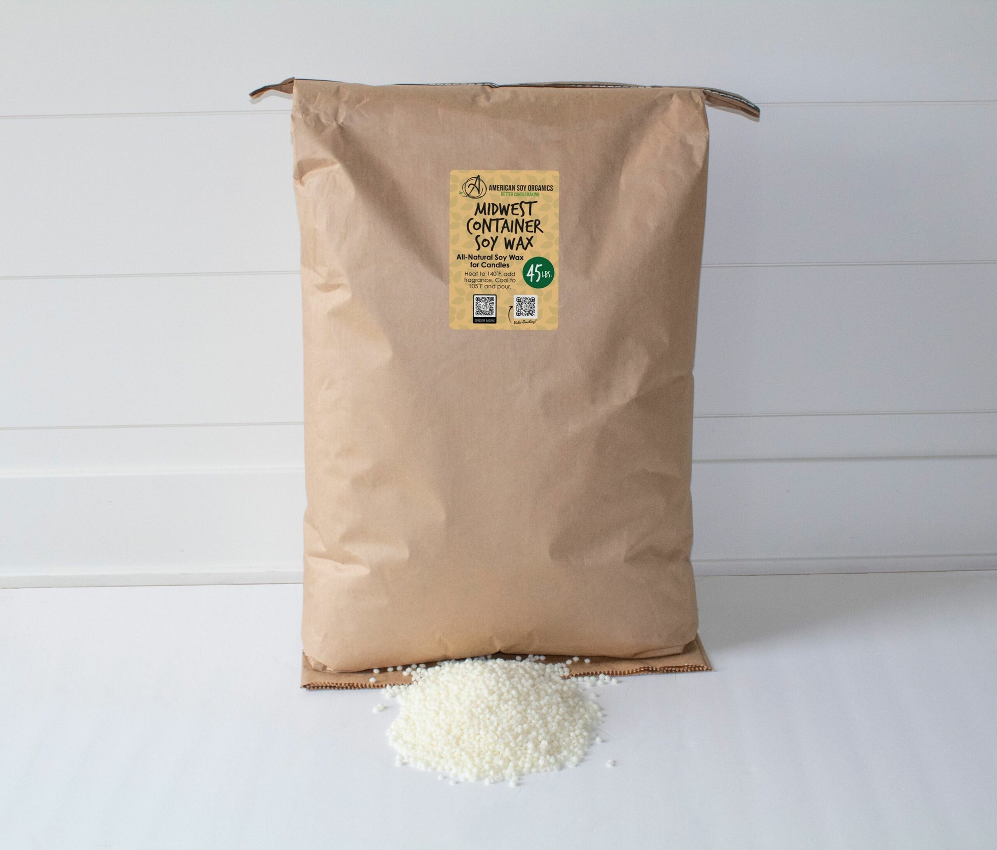 A brown bag labeled '45 lbs. Midwest Container Soy Wax' with a small amount of white soy wax beads spilled in front of the bag on a white surface