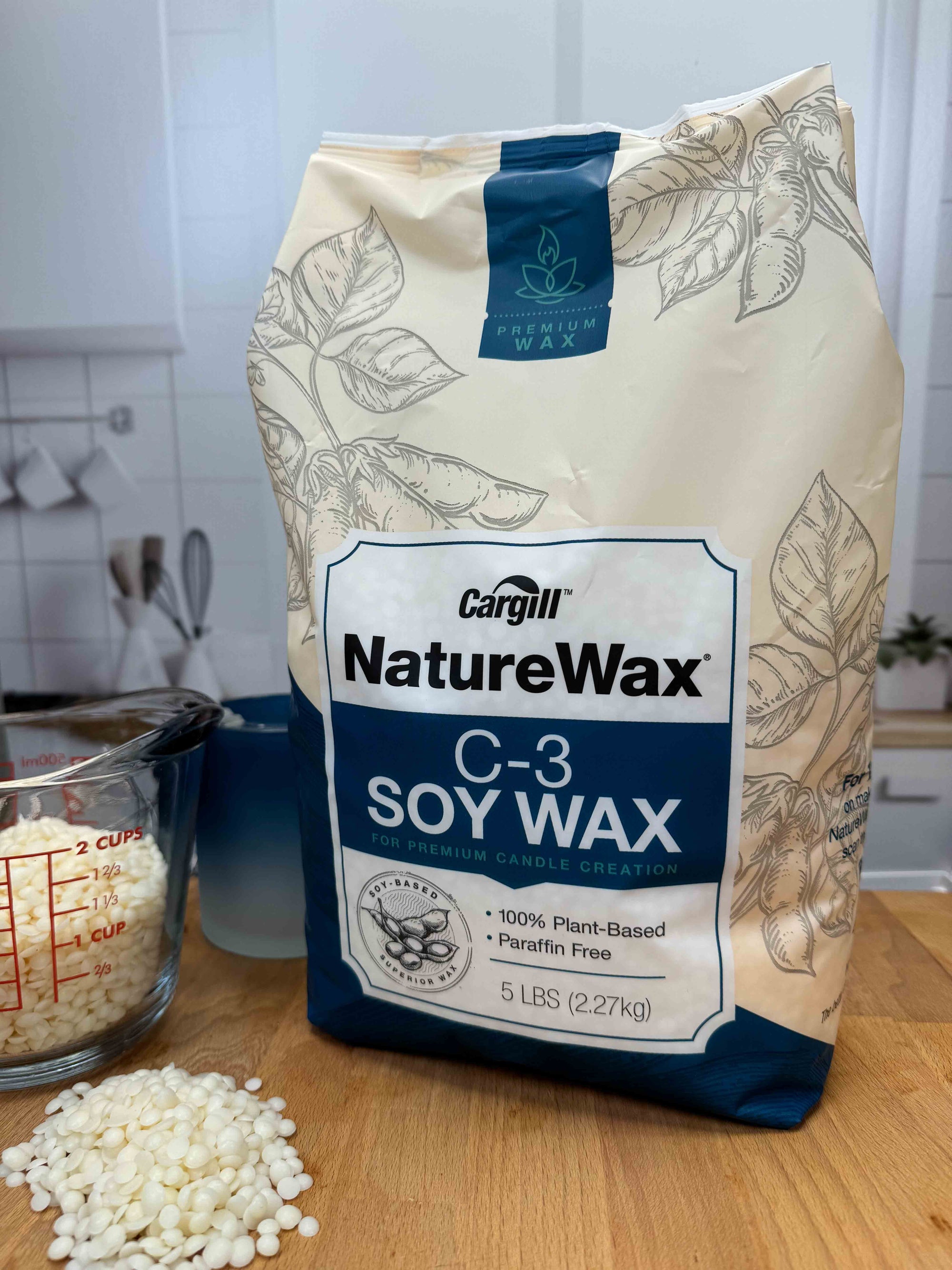 Bag of Cargill NatureWax C-3 Soy Wax on a wooden surface with wax beads beside it, with a kitchen background