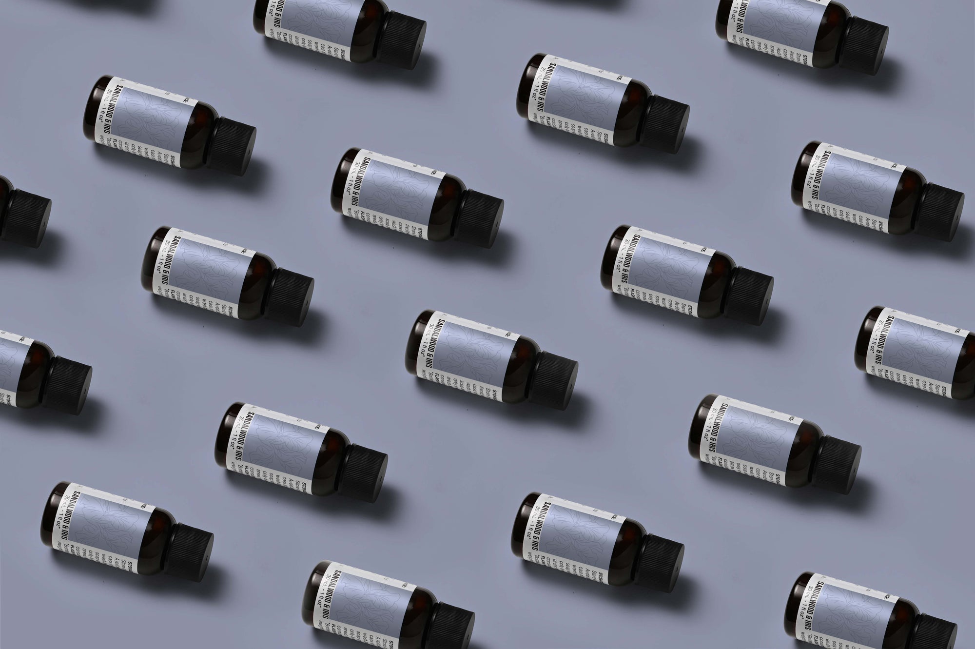 Pattern of Sandalwood & Iris fragrance oil bottles on a dusty blue background