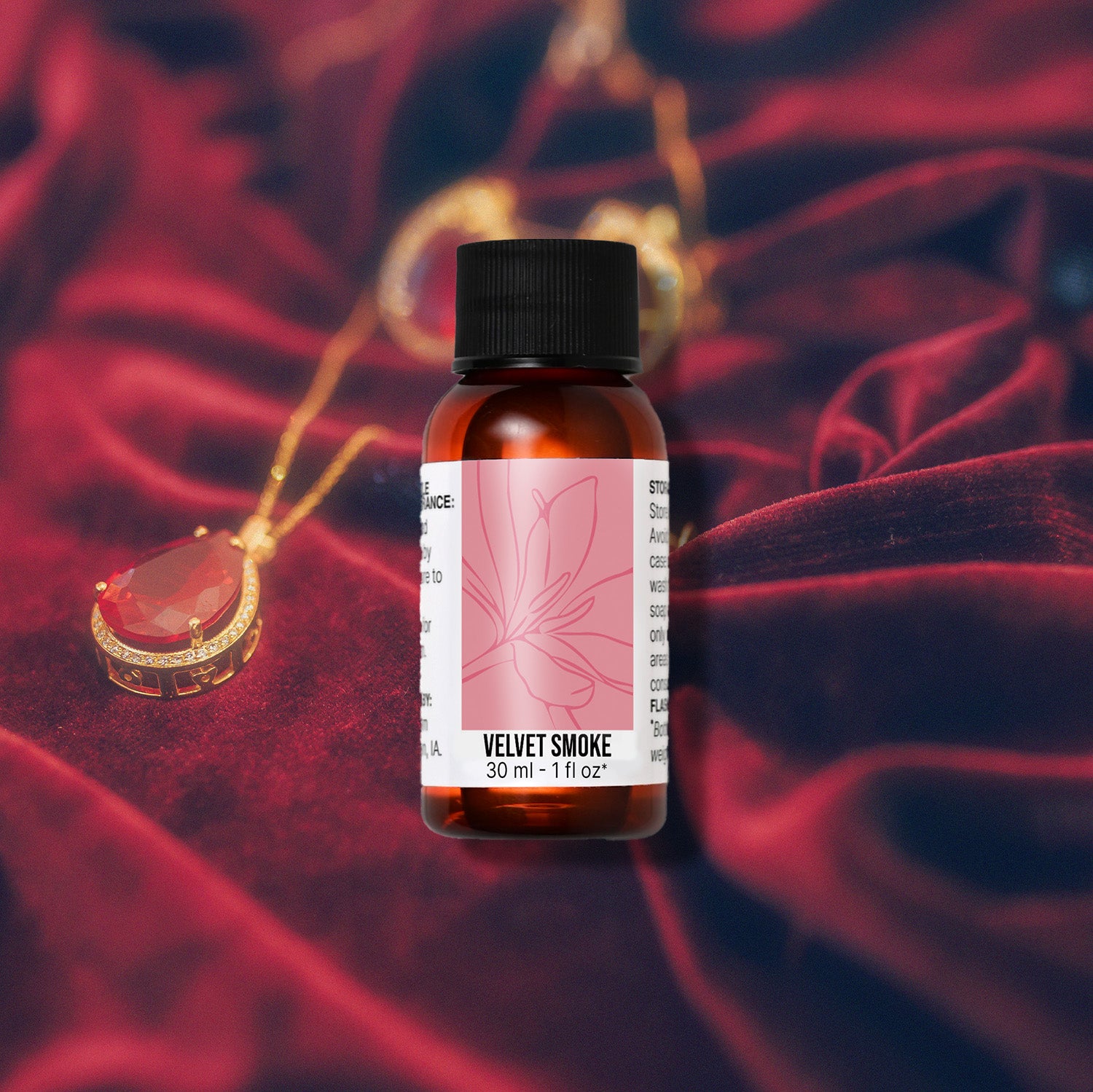 Bottle of 'Velvet Smoke' fragrance oil with a red pendant necklace on a textured red fabric background