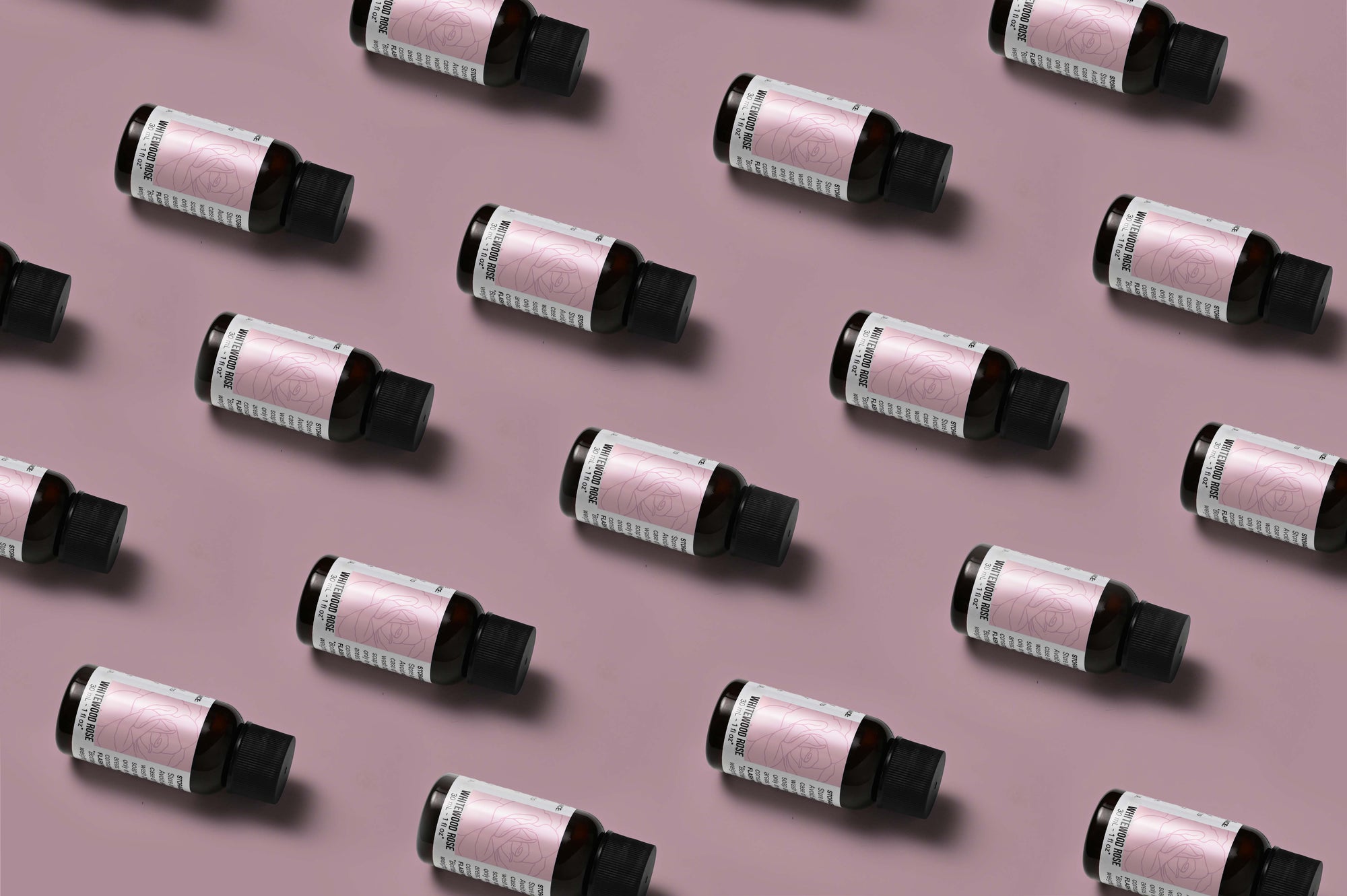 Pattern of Whitewood Rose fragrance oil bottles on a light rose background