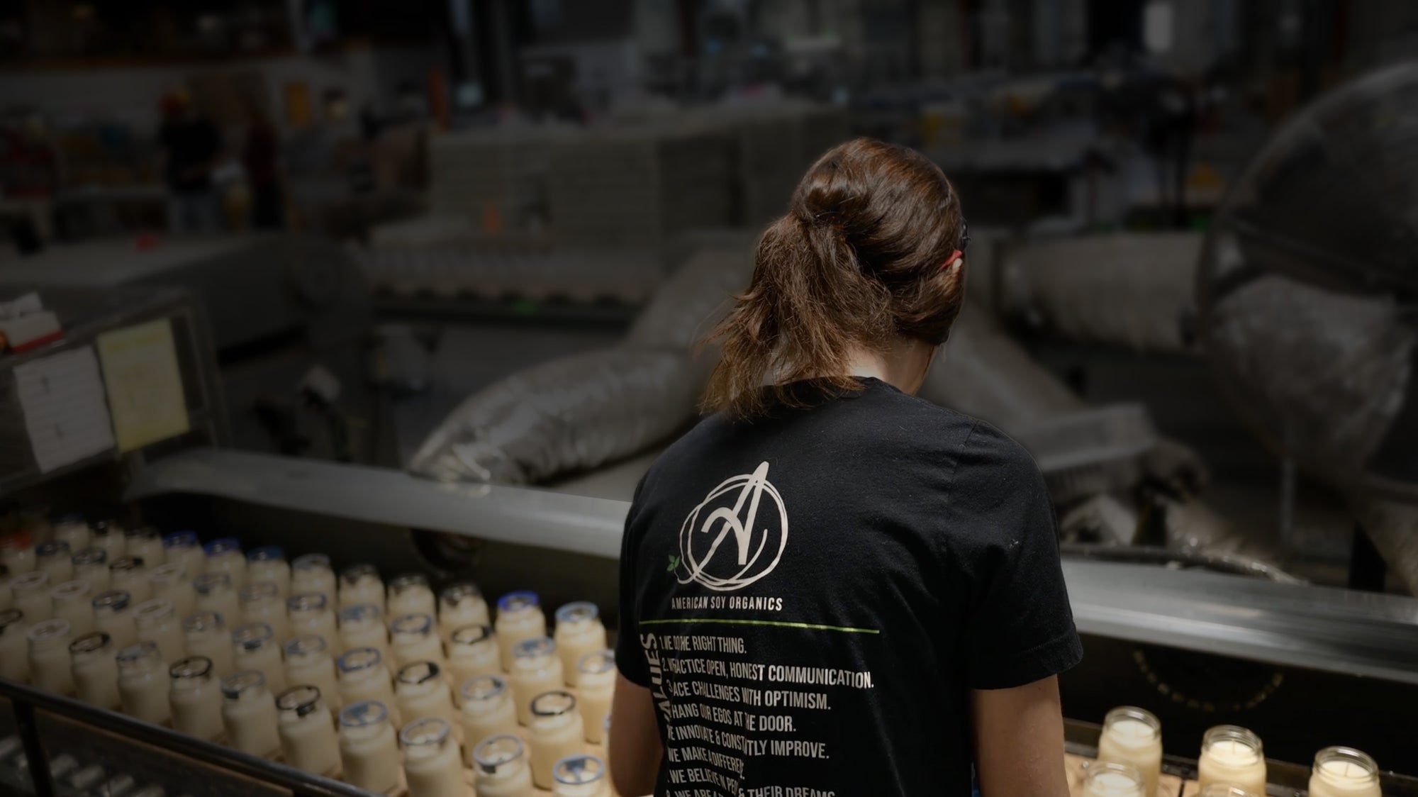 Person wearing a black t-shirt with a logo and text, standing in a warehouse setting.
