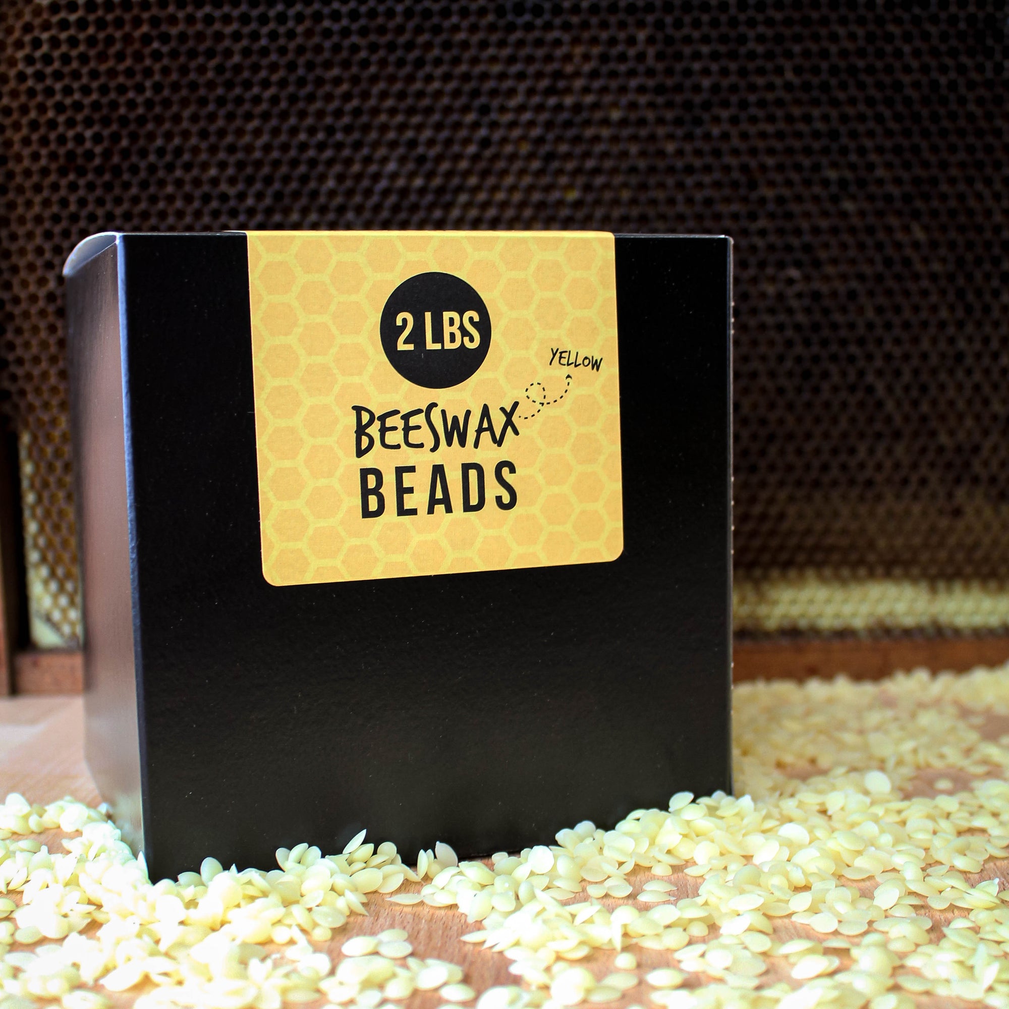 Box of yellow beeswax beads with a label indicating '2 LB Yellow Beeswax Beads' on a honeycomb background.
