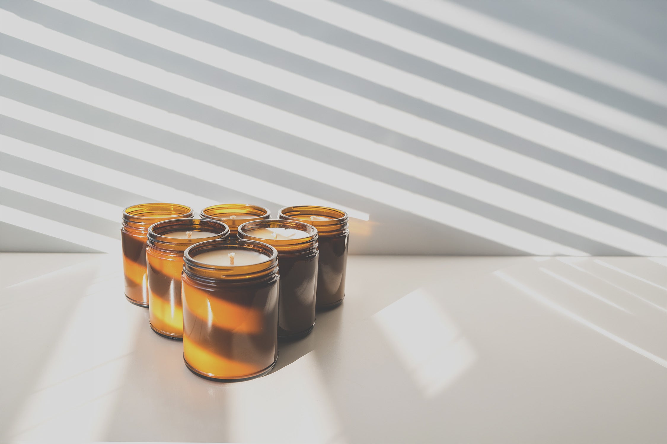 Set of five amber glass candles with wicks on a white surface with a striped background