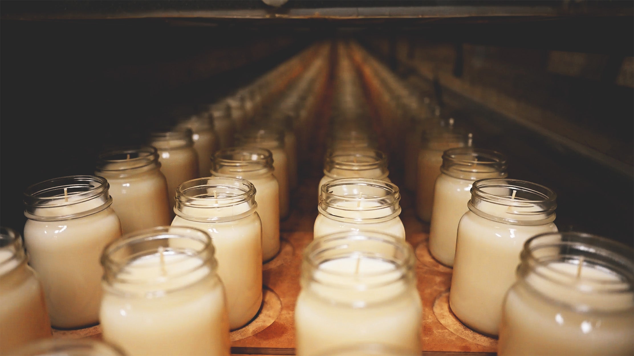Row of candles in glass jars on a production line.