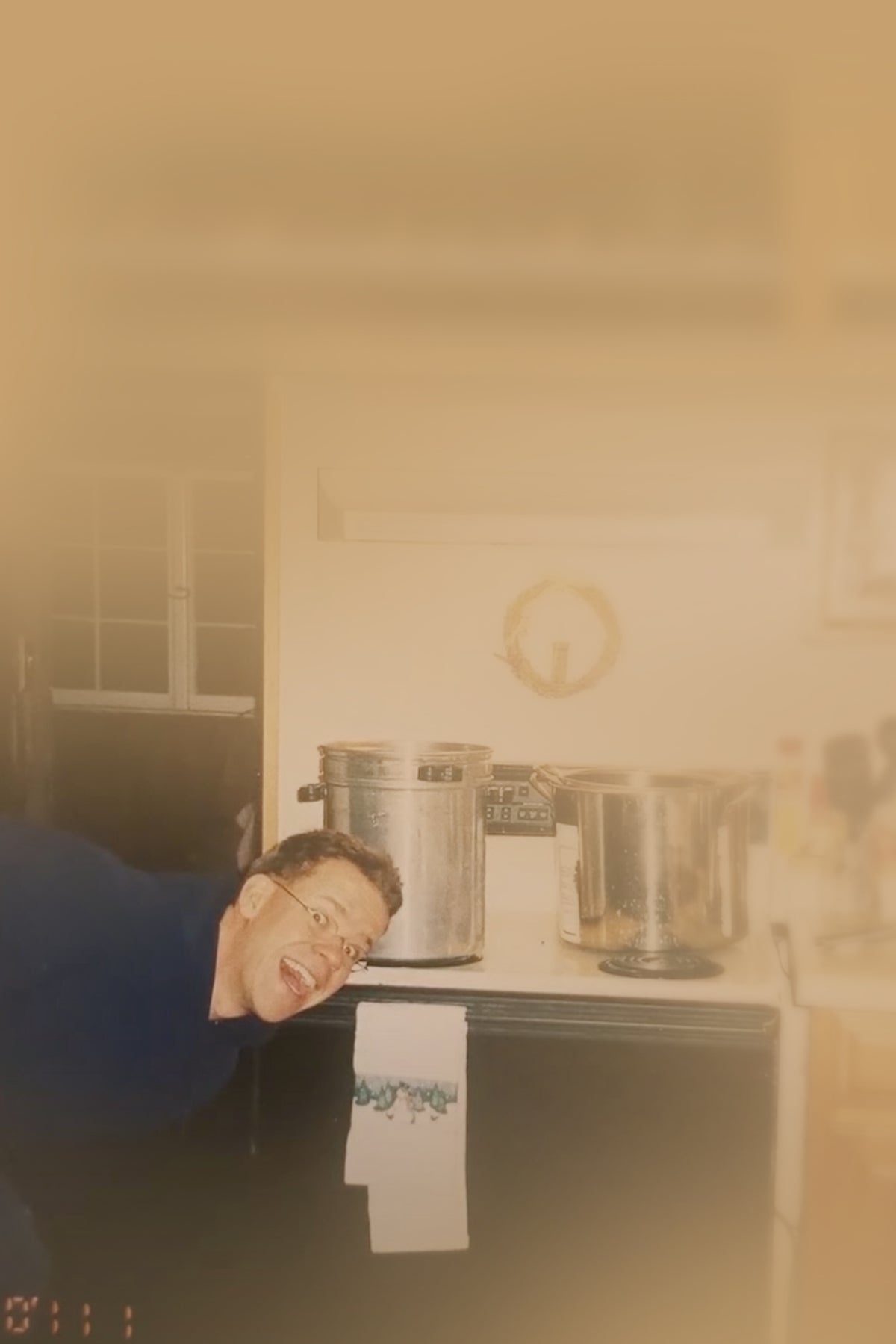 Person leaning over a kitchen counter with pots and pans in the background