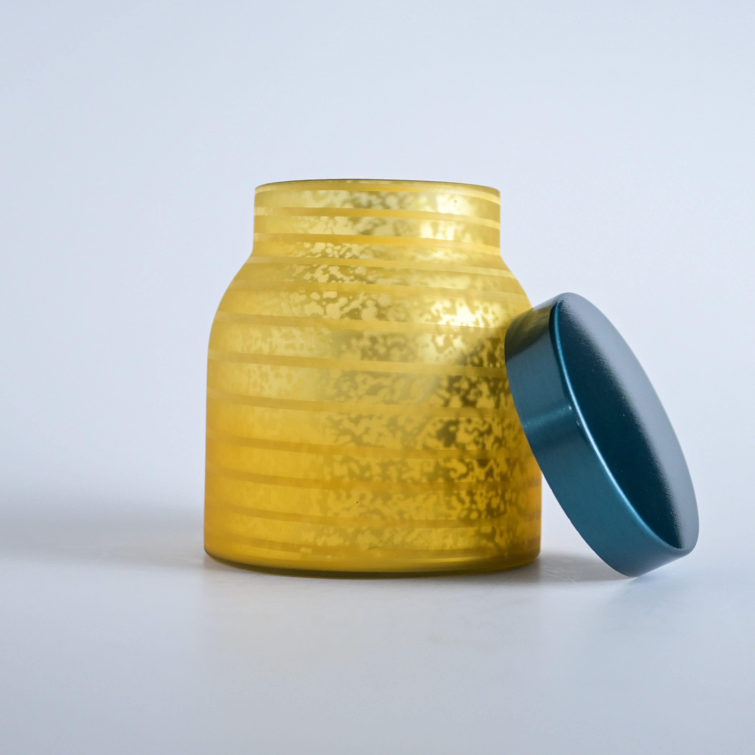 Golden yellow striped jar with a teal lid on a white background