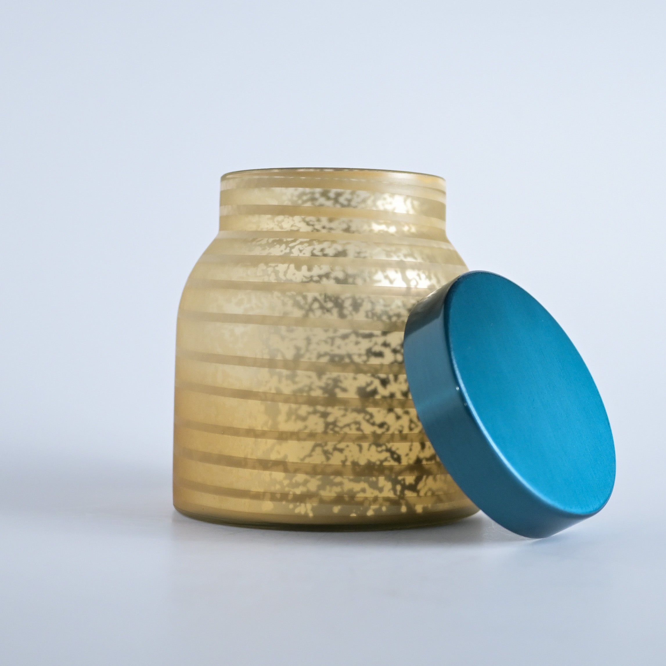 Gold striped jar with a teal lid on a white background