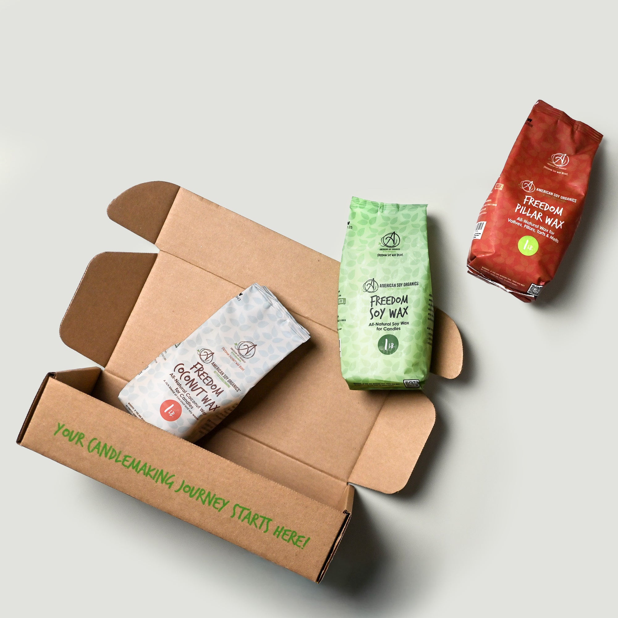 Candle-making supplies including a cardboard box, green and red packages on a light gray background.