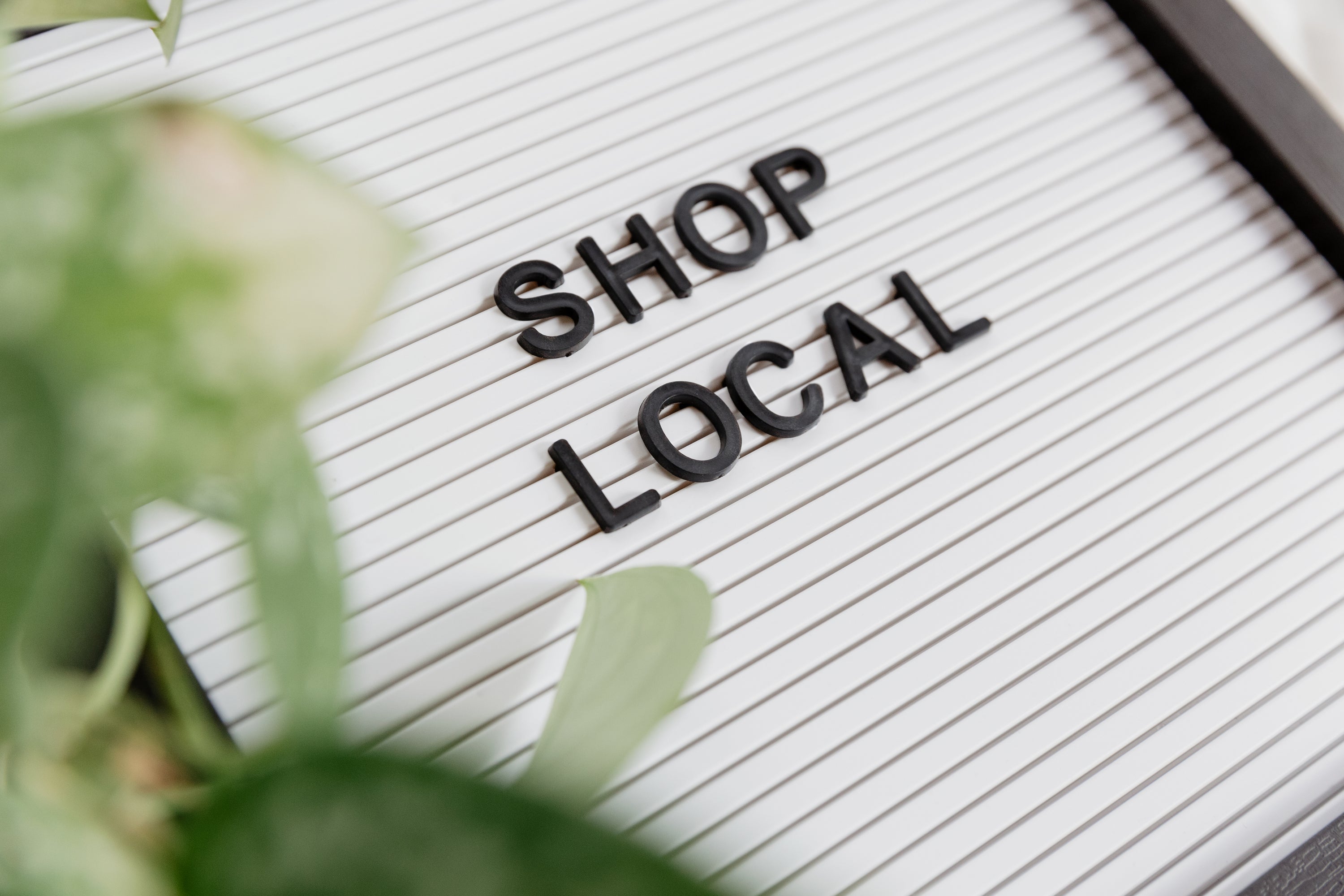 A shop local letterboard with blurred green foliage