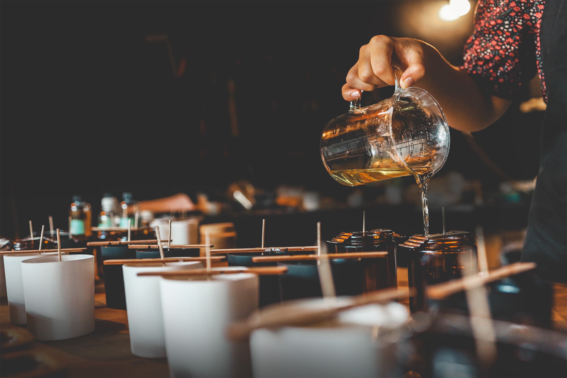 Person pouring wax into small cups on a dark background