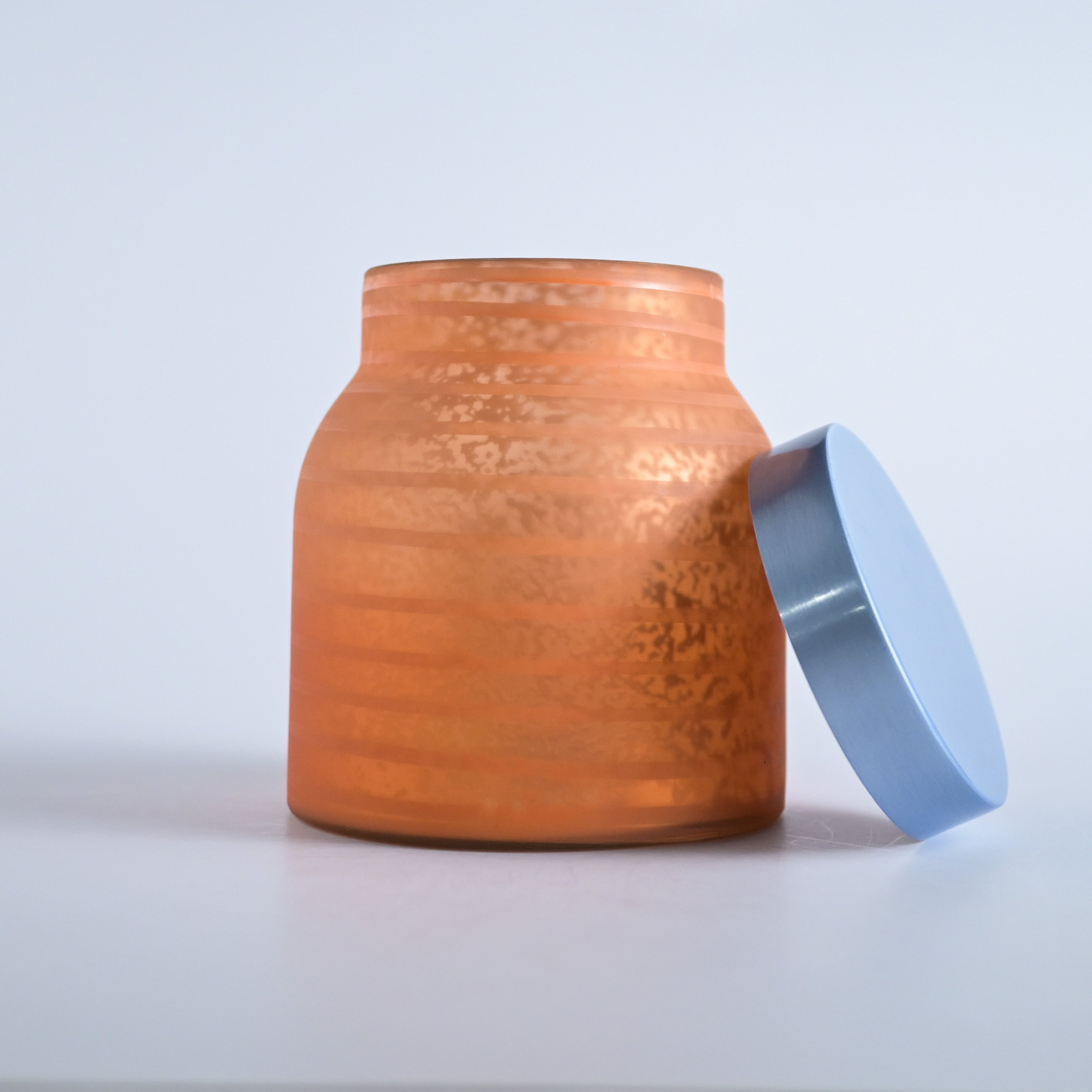 Orange striped jar with a silver lid on a white background