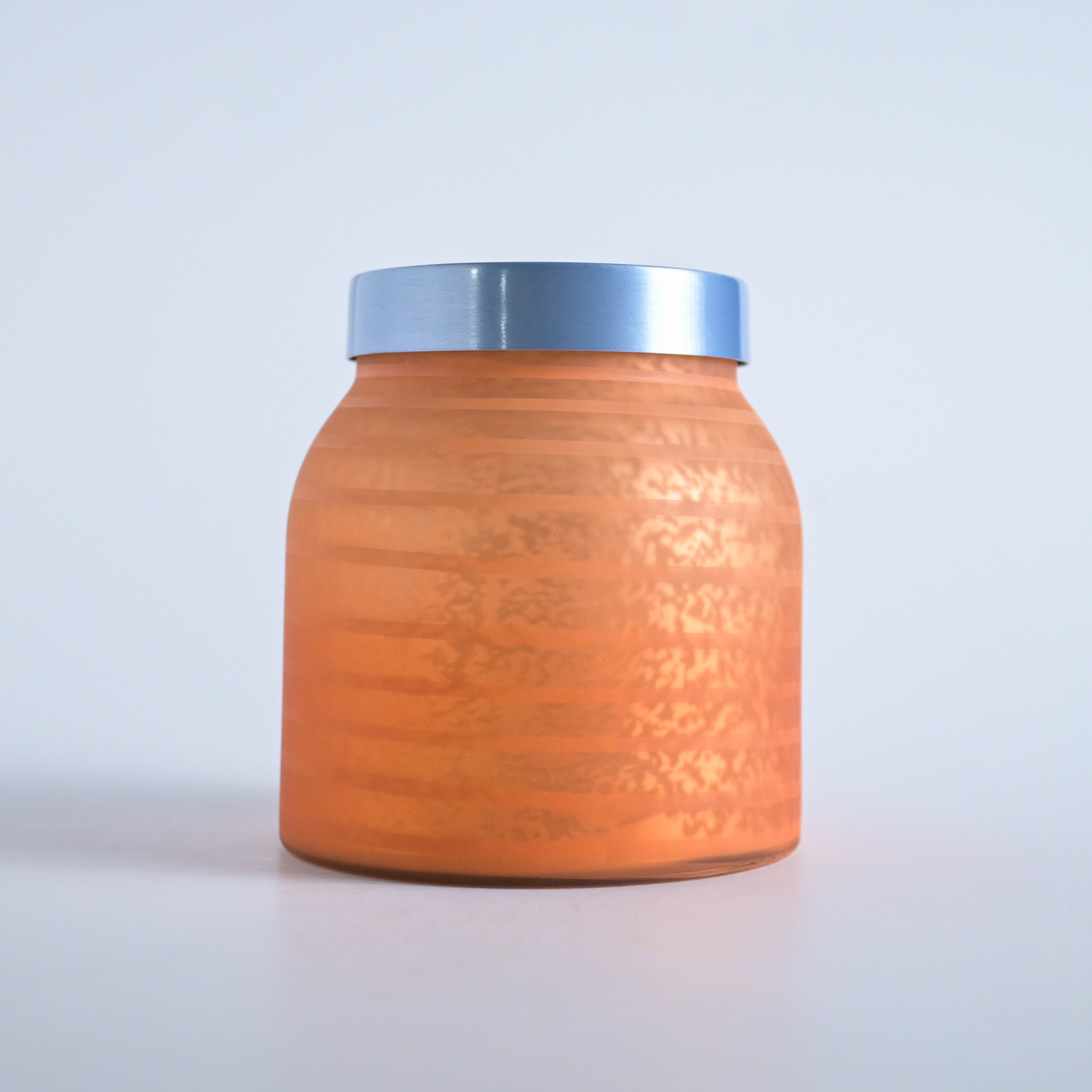 Orange striped jar with a silver lid on a white background