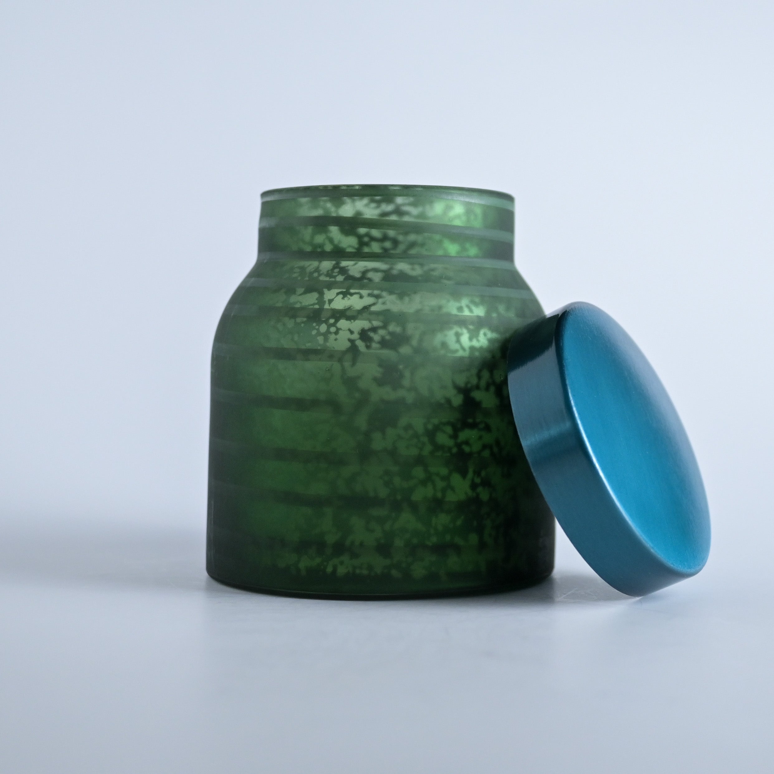 Dark green striped jar with a teal lid on a white background