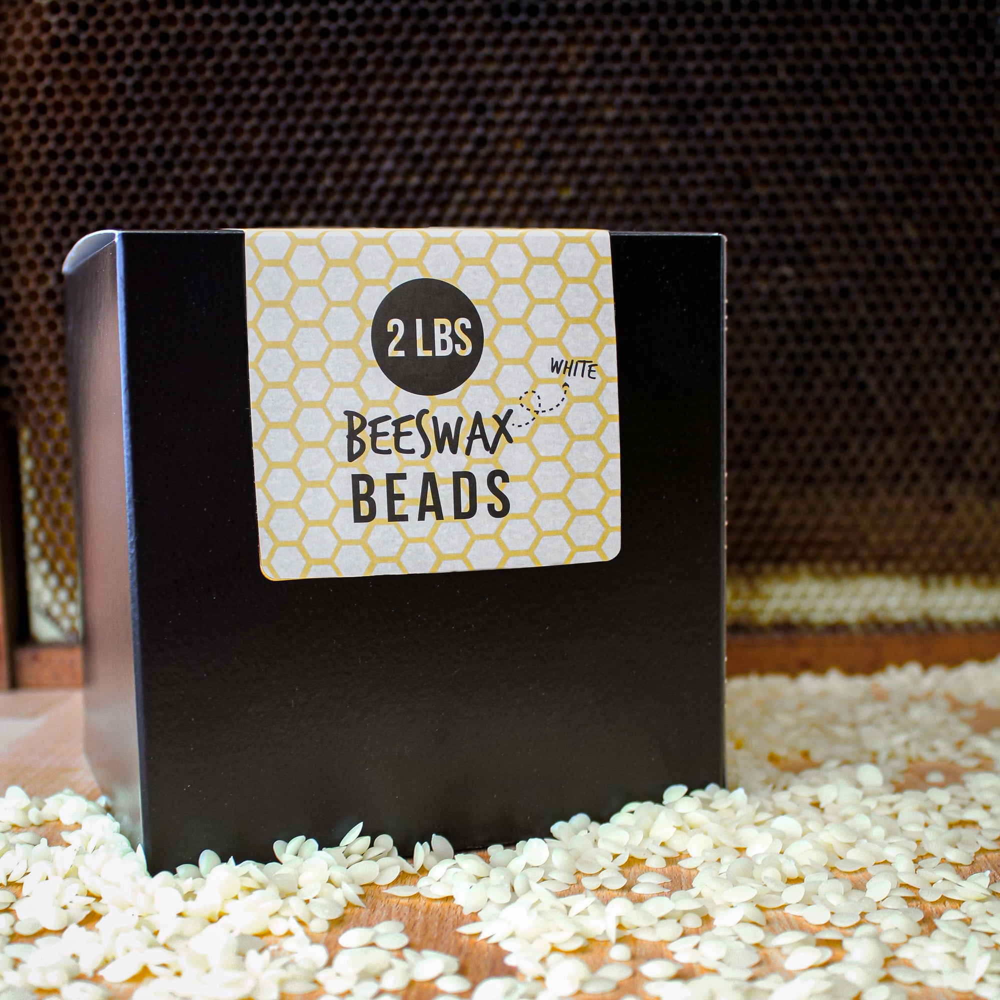 Box of white beeswax beads with a label indicating '2 LB White Beeswax Beads' on a honeycomb background.