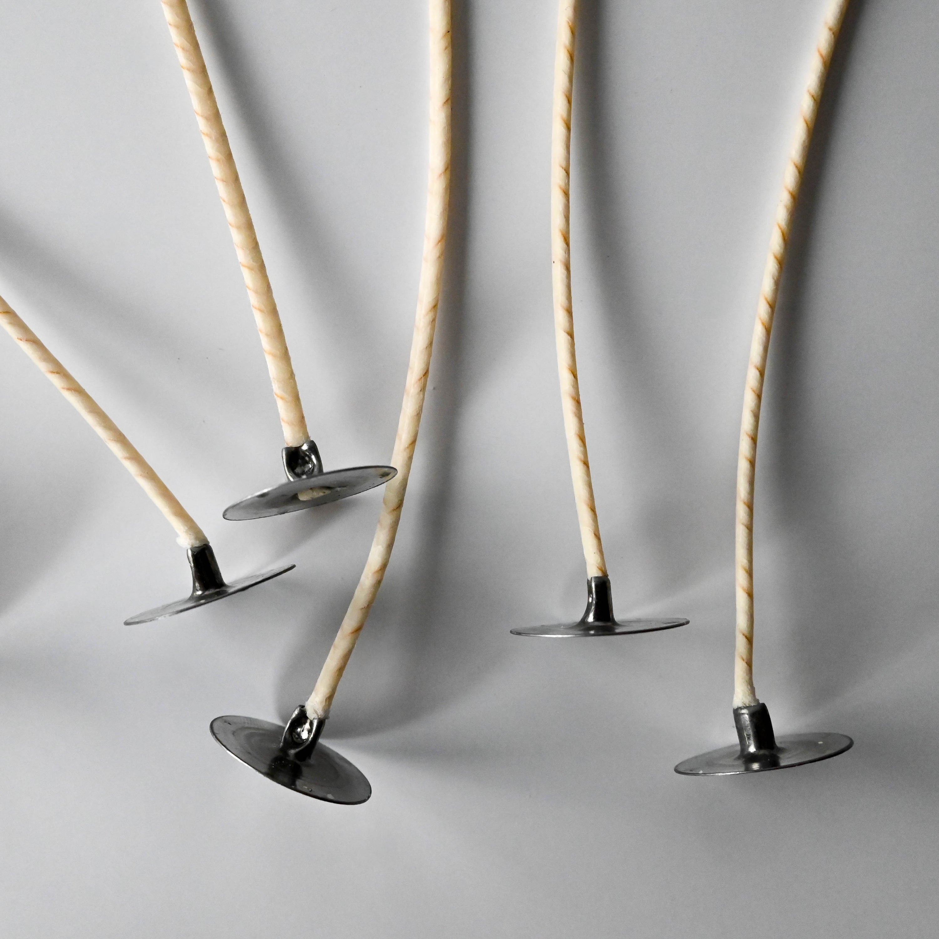 A collection of thin, twisted candle wicks positioned vertically on a white background